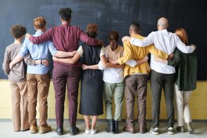 A diverse group of adults in casual outfits hugging in front of a chalkboard, symbolizing teamwork.